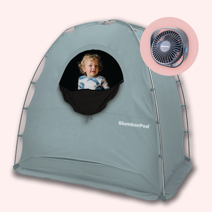 A light blue SlumberPod portable sleep tent for toddlers, featuring a black mesh window where a smiling young boy is visible. The tent has a sturdy, arched frame and the 'SlumberPod' logo printed in white near the bottom. In the upper right corner, a circular inset shows a dark gray portable fan designed to fit the tent's integrated fan pocket.