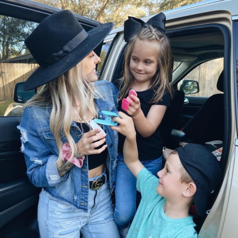Woman with a large black hat interacting with two children in a car.
