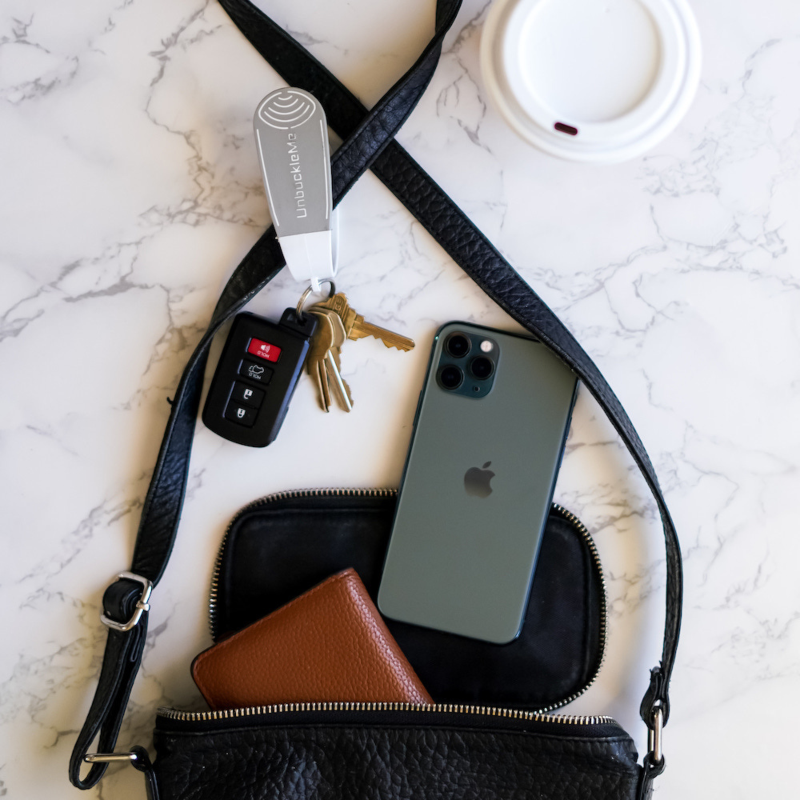 Black crossbody bag with phone, wallet, keys, and car key fob on a marble surface