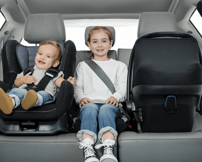 Two children in car seats in a car's back seat.