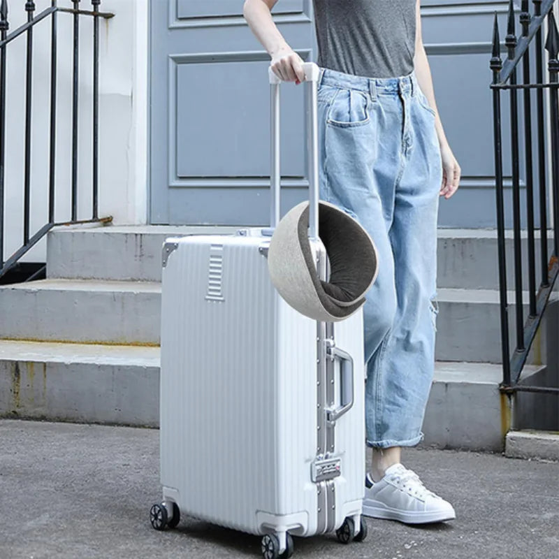 Gray travel neck pillow attached to the handle of a white rolling suitcase.