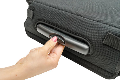 A close-up studio shot of the back of a black fabric travel bag. A hand with pink nail polish is shown pressing the release button on a sturdy, integrated black plastic carrying handle. The handle is recessed into the fabric casing, highlighting the portable and user-friendly design of the product.