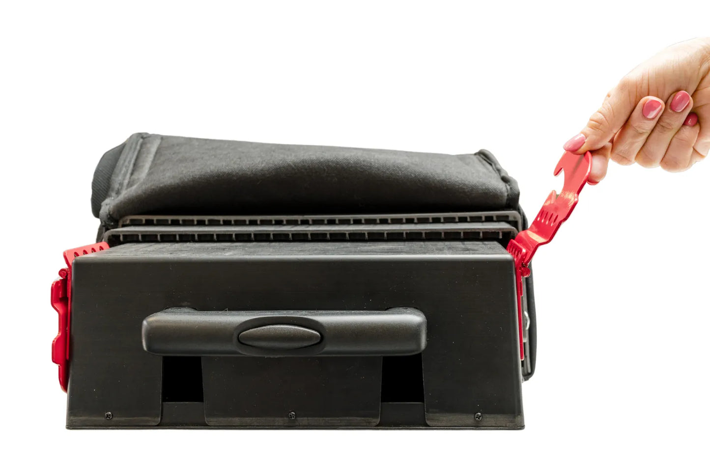 A close-up studio shot of the black base of the TelePort booster seat. A hand with pink nail polish is shown pulling upward on a red metal seat belt positioning clip on the right side of the device. The base features a sturdy plastic housing with a built-in handle and a folded black fabric section on top.